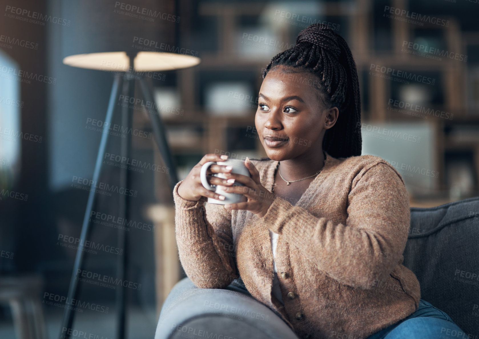 Buy stock photo Cropped shot of an attractive young woman sitting alone in her living room and enjoying a cup of coffee