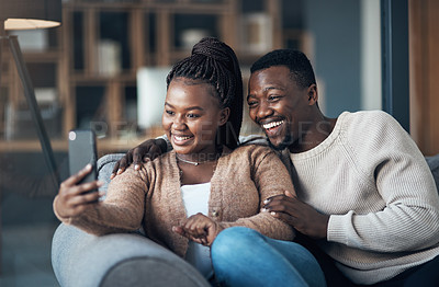 Buy stock photo Cropped shot of a happy young couple sitting together and using a cellphone to take a selfie at home