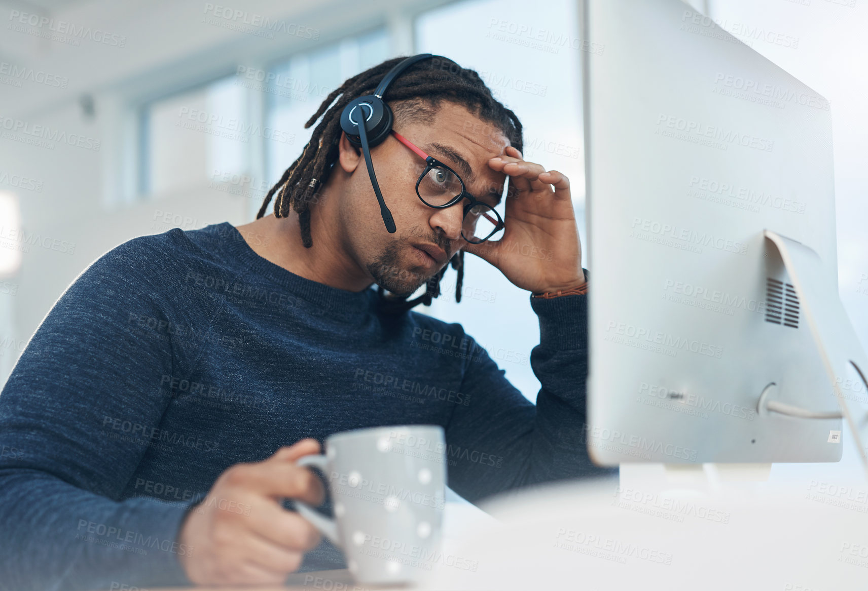 Buy stock photo Shot of a young businessman wearing a headset and looking stressed out while working on a computer in an office