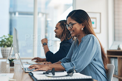 Buy stock photo Shot of a young businesswoman working on a laptop in an office with her colleague in the background