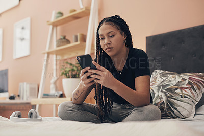 Buy stock photo Shot of a young woman using a smartphone while relaxing on her bed at home