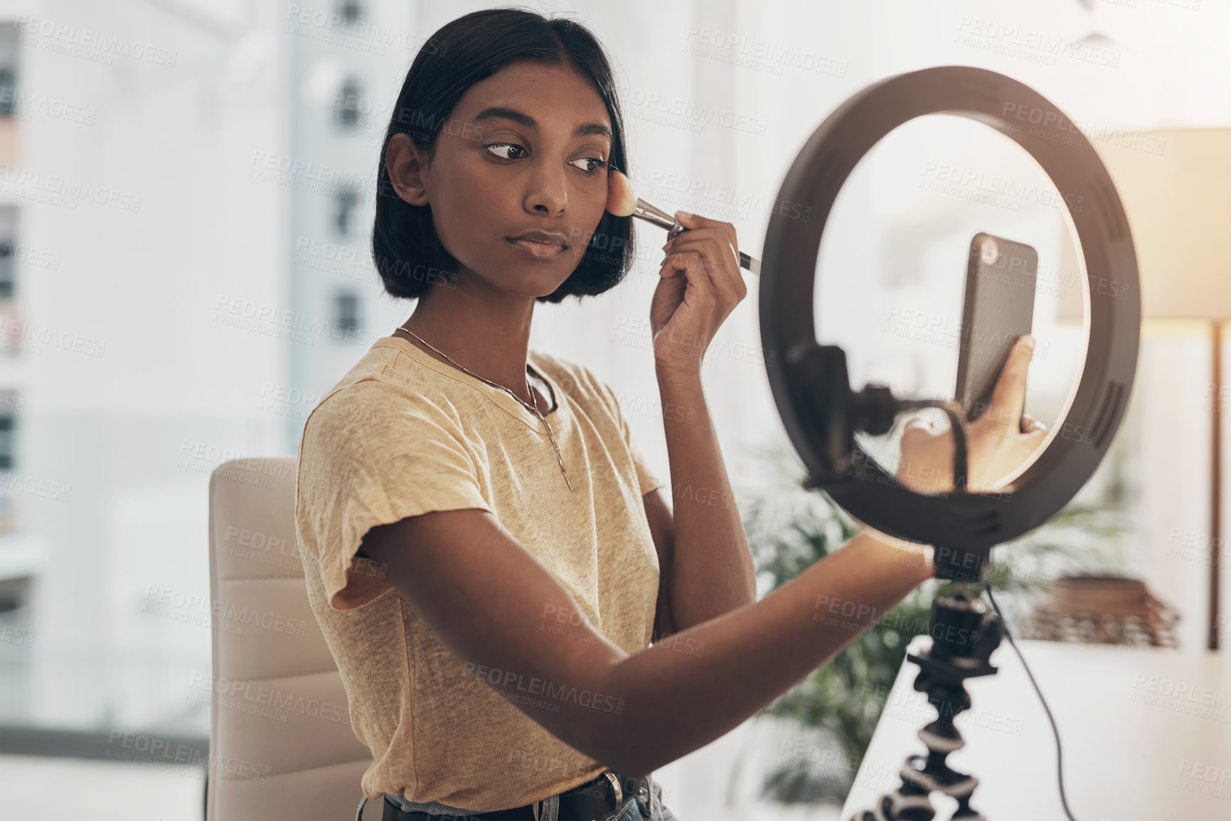 Buy stock photo Shot of a young woman applying makeup while filming a beauty tutorial at home