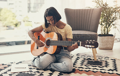 Buy stock photo Shot of a young woman playing the guitar at home