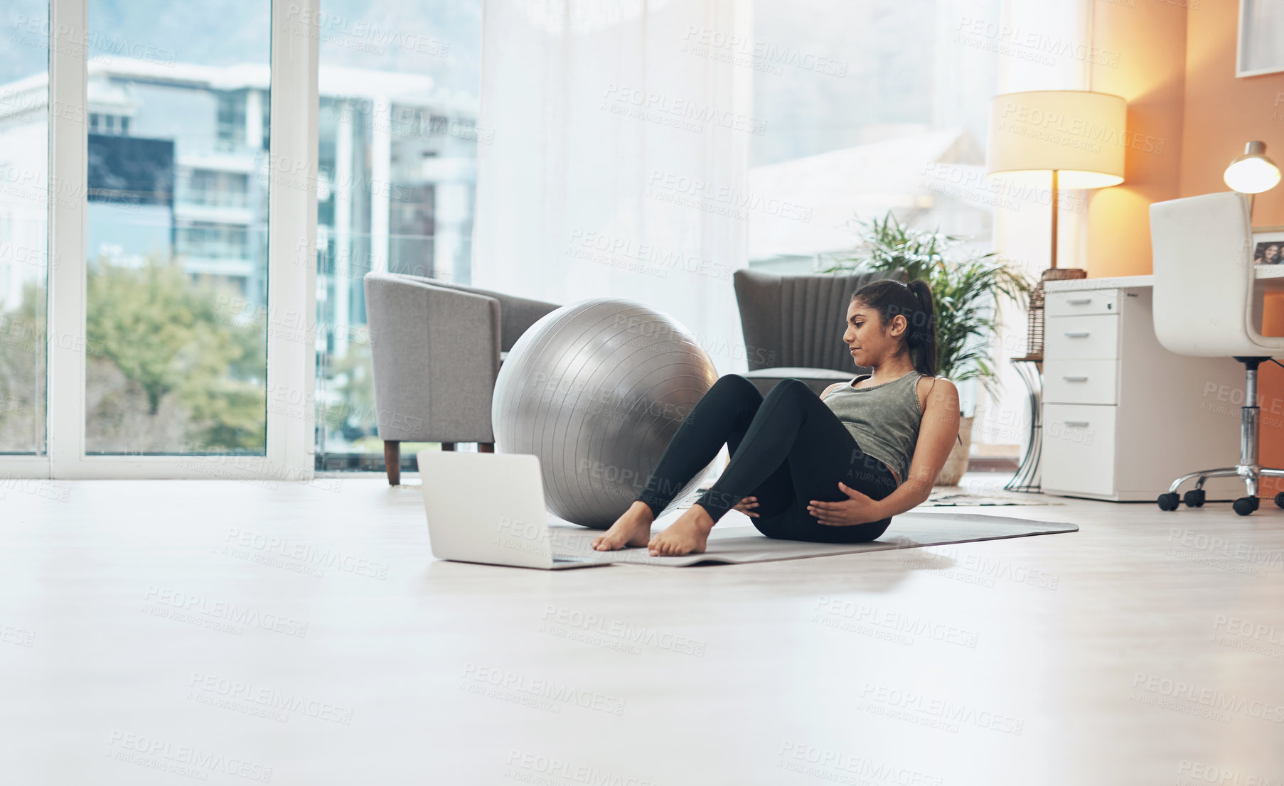 Buy stock photo Shot of a woman working out in her living room with her laptop in front of her