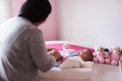 Buy stock photo Shot of a young woman changing her baby girl’s clothing at home