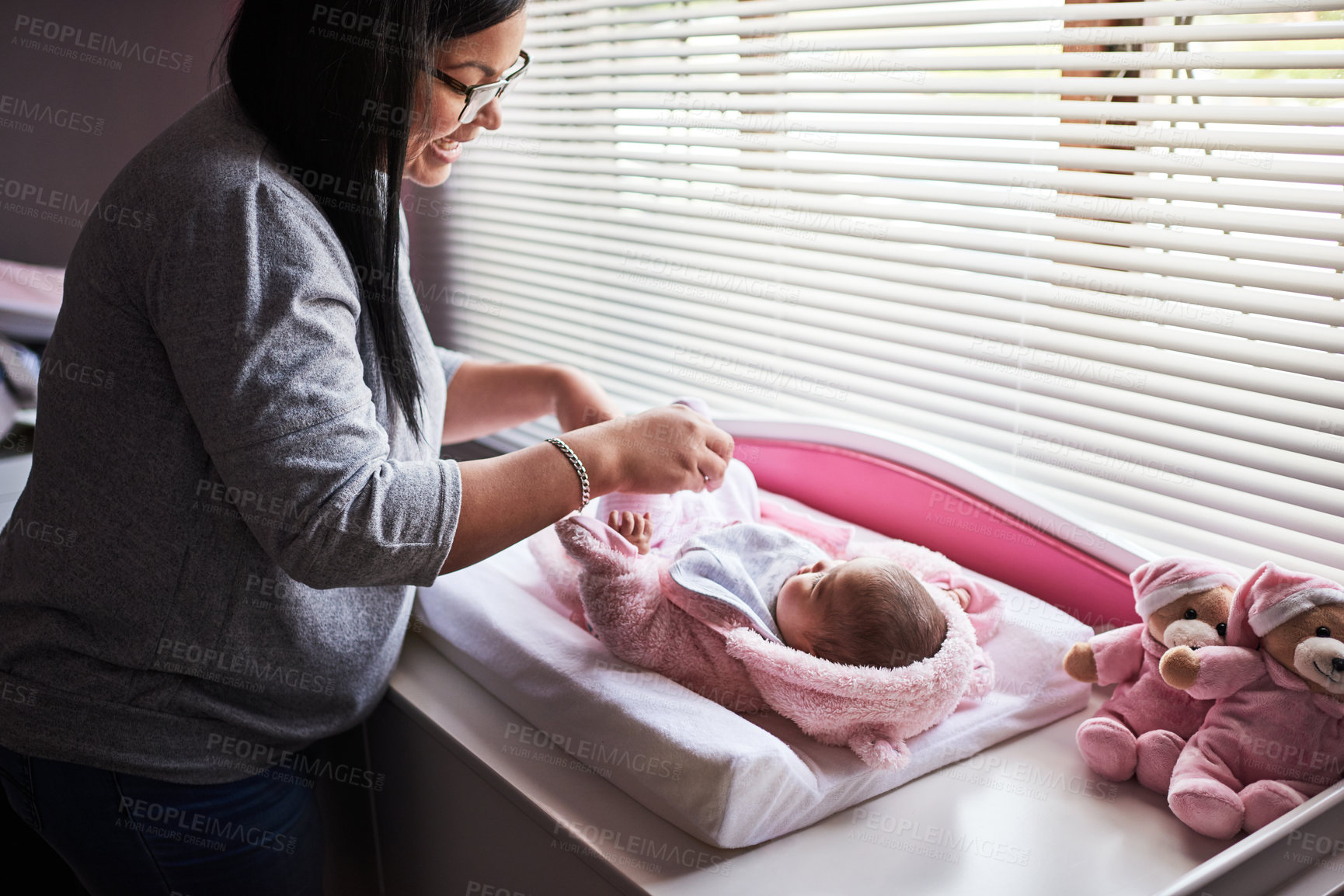 Buy stock photo Shot of a young woman changing her baby girl’s clothing at home