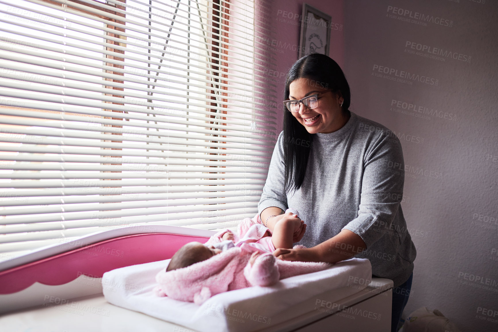 Buy stock photo Shot of a young woman changing her baby girl’s clothing at home