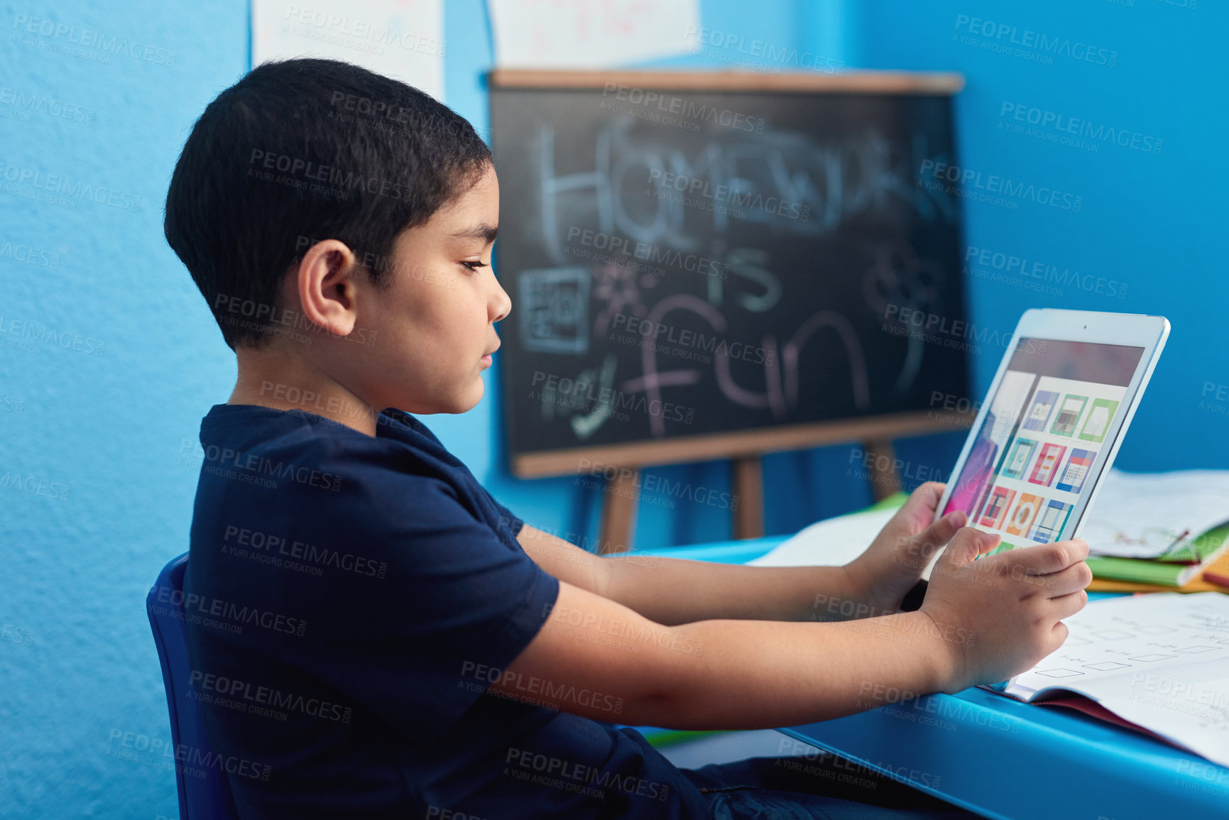 Buy stock photo Shot of an adorable little boy using a digital tablet to complete a school assignment at his desk