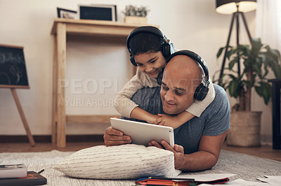 Buy stock photo Shot of an adorable little boy using a digital tablet and headphones with his father at home