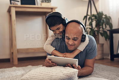 Buy stock photo Shot of an adorable little boy using a digital tablet and headphones with his father at home