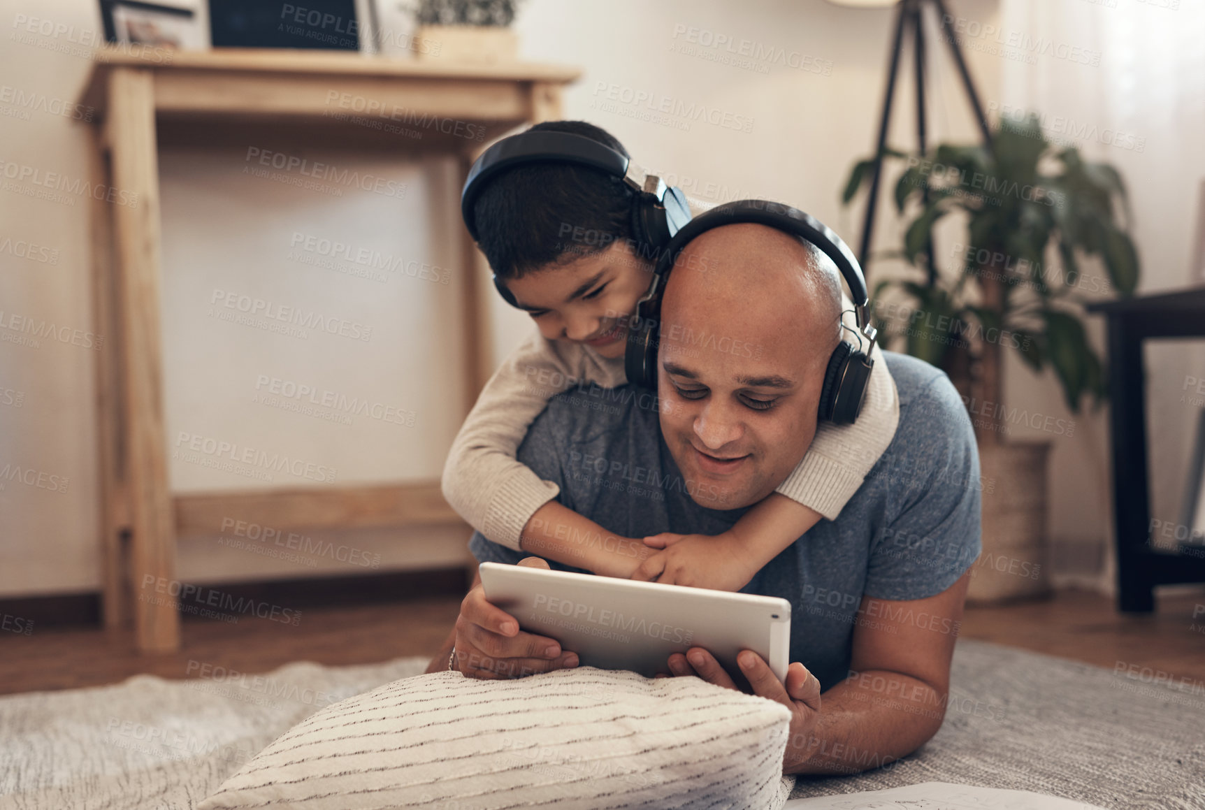 Buy stock photo Shot of an adorable little boy using a digital tablet and headphones with his father at home