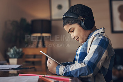 Buy stock photo Shot of an adorable little boy using a digital tablet and headphones while completing a school assignment at home