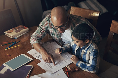 Buy stock photo Shot of an adorable little boy using a digital tablet while completing a school assignment with his father at home