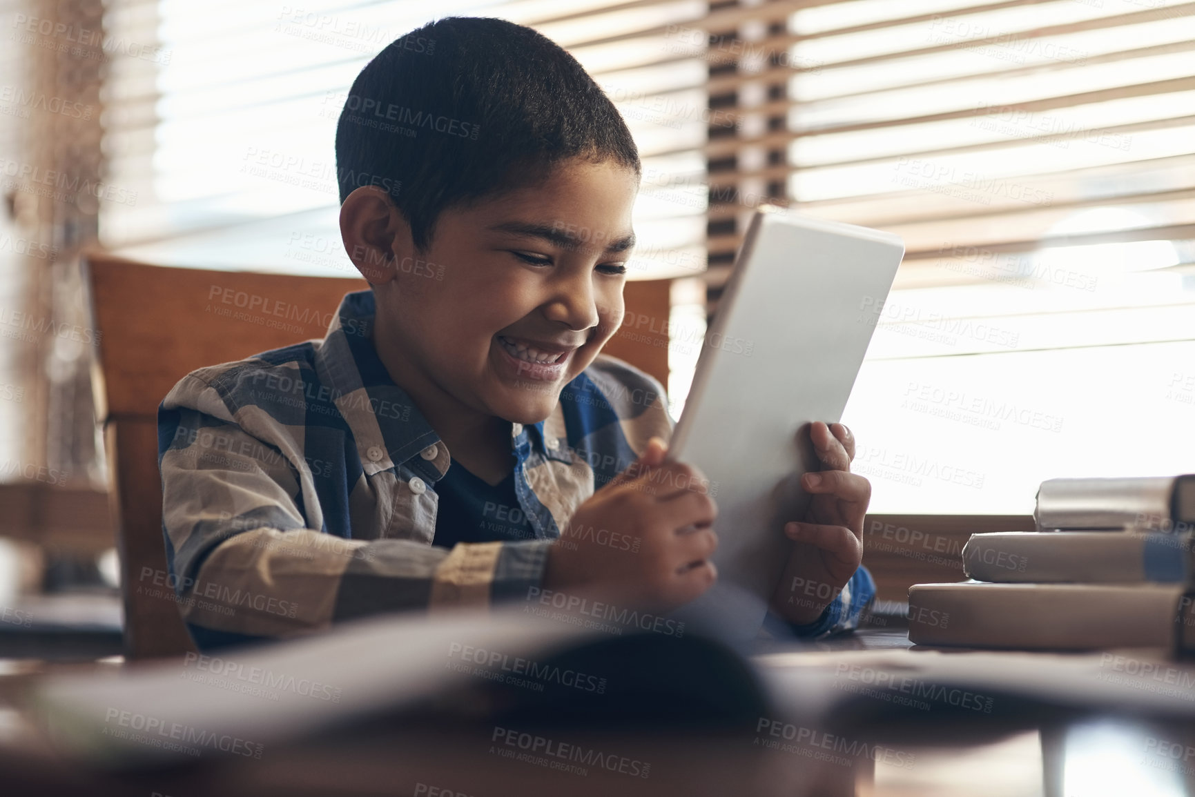 Buy stock photo Shot of an adorable little boy using a digital tablet while completing a school assignment at home