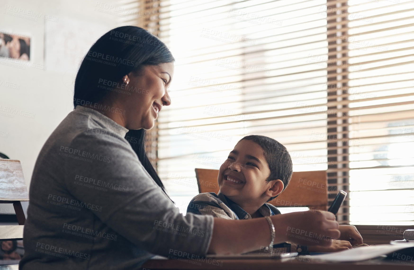 Buy stock photo Shot of an adorable little boy using a magnifying glass while completing a school assignment with his mother at home