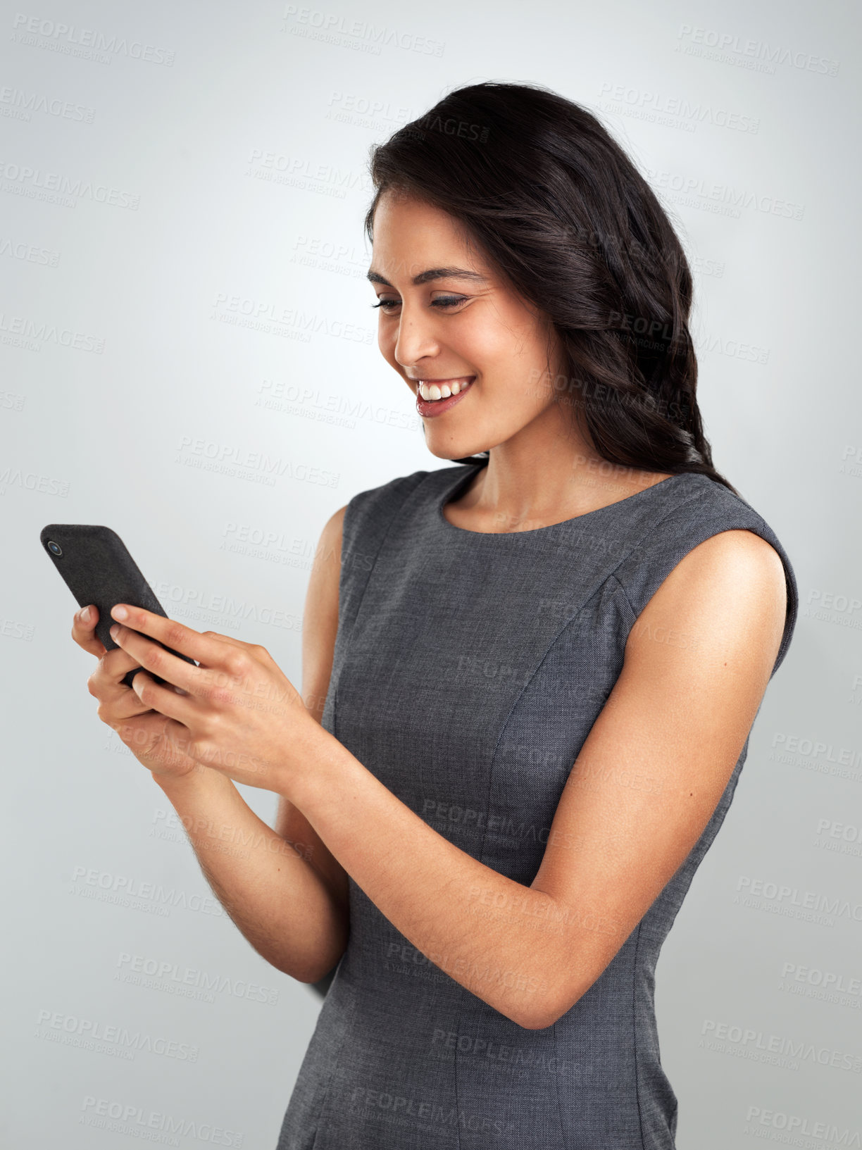 Buy stock photo Shot of a young woman using her cellphone while standing against a grey background