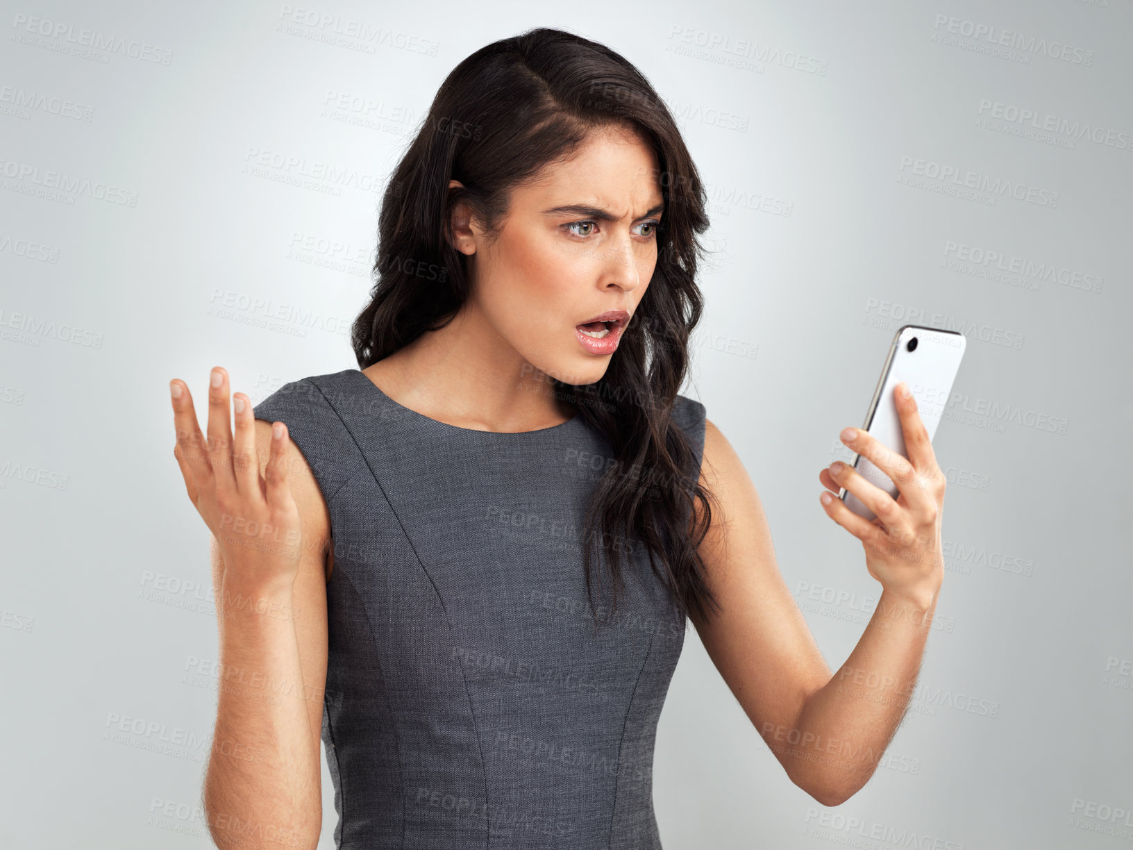 Buy stock photo Shot of a young woman using her cellphone while standing against a grey background