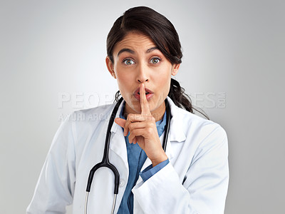 Buy stock photo Studio portrait of a young doctor with her finger on her lips against a grey background