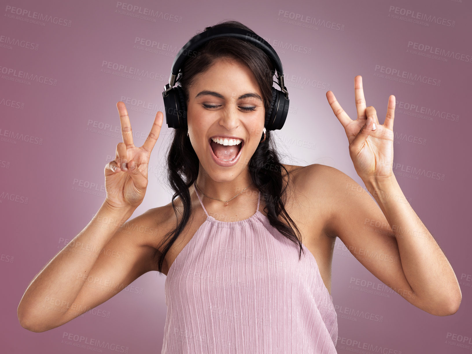 Buy stock photo Shot of a beautiful young woman showing the peace sign while listening to music wearing headphone against a pink background