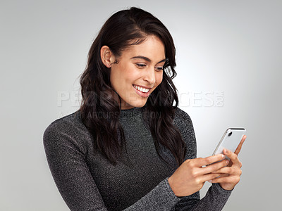 Buy stock photo Shot of a young woman using her cellphone while standing against a grey background