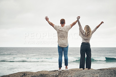 Buy stock photo Rearview shot of a couple standing with their arms raised at the beach