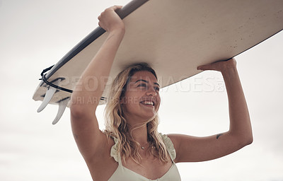Buy stock photo Shot of a young woman carrying his surfboard on her head while at the beach