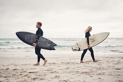 Buy stock photo Shot of two people walking on the beach with their surfboards