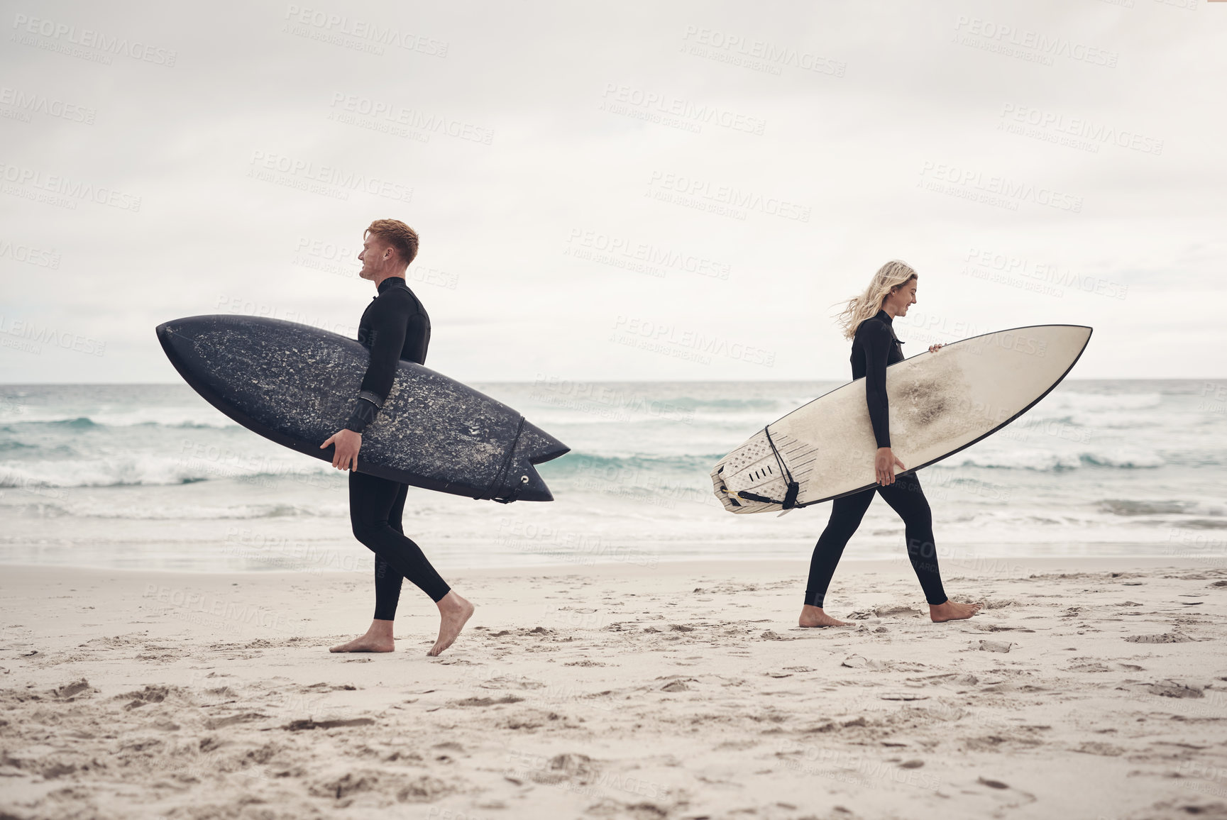 Buy stock photo Shot of two people walking on the beach with their surfboards