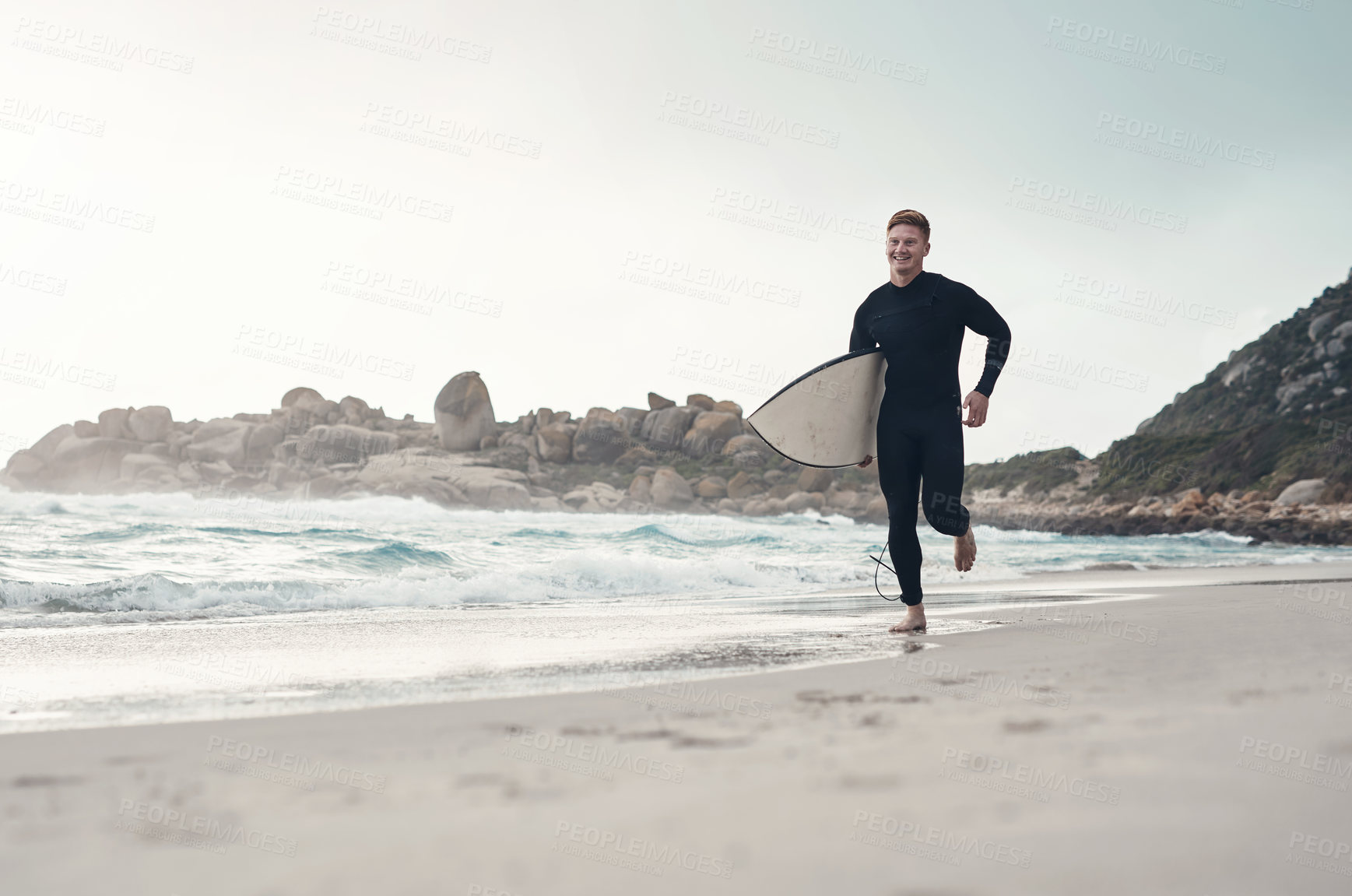 Buy stock photo Shot of a young man along the shoreline with his surfboard