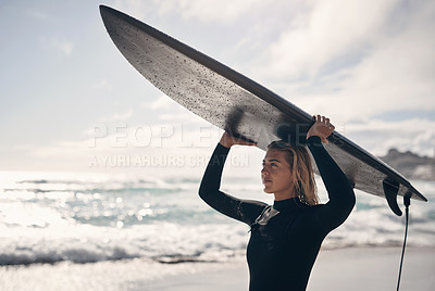 Buy stock photo Shot of a young woman carrying his surfboard on her head while at the beach