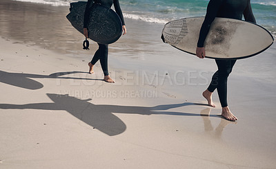 Buy stock photo Cropped shot of two people carrying surfboards while walking on the beach