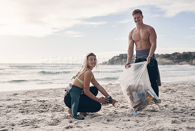 Buy stock photo Shot of a young couple doing a beach clean while wearing wetsuits
