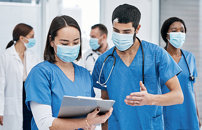 Buy stock photo Shot of two medical practitioners going through notes in a busy hospital