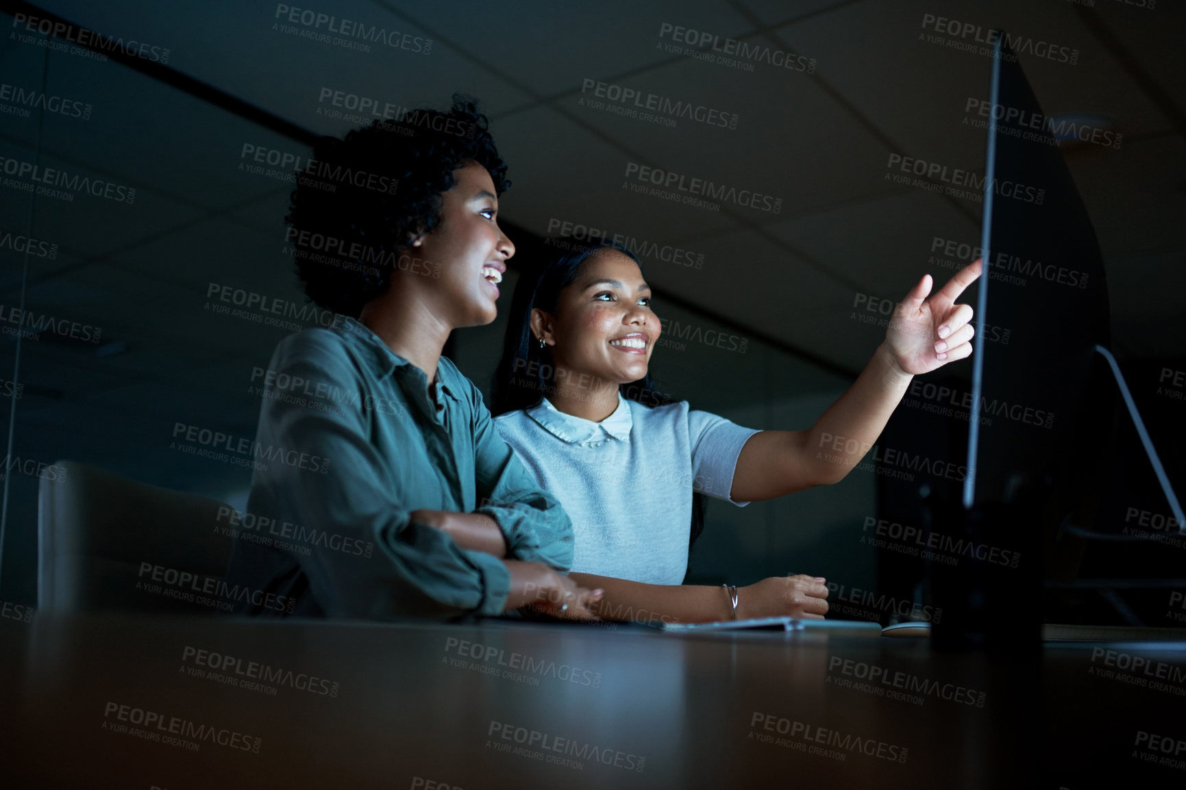 Buy stock photo Shot of two young businesswomen using a computer together during a late night at work