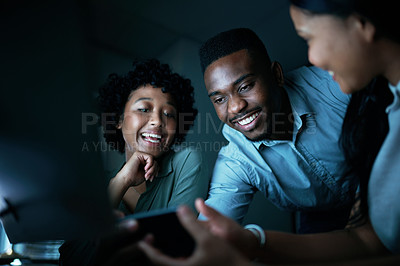 Buy stock photo Shot of a group of young businesspeople using a smartphone and computer together during a late night at work