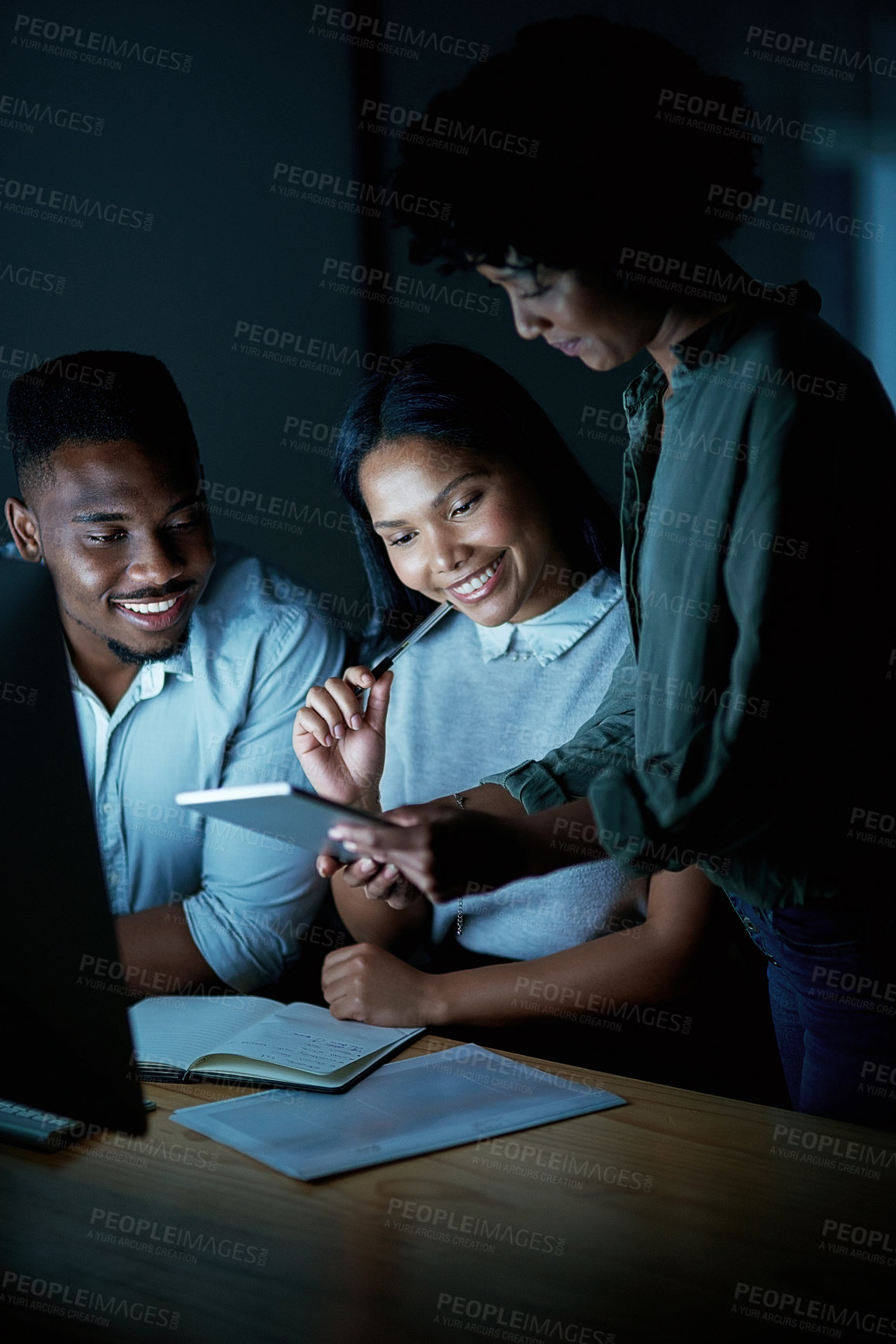 Buy stock photo Shot of a group of young businesspeople using a digital tablet and computer during a late night at work