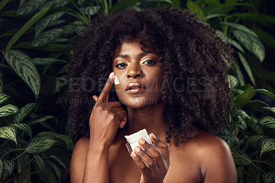 Buy stock photo Shot of a beautiful young woman applying moisturiser to her face against a leafy background