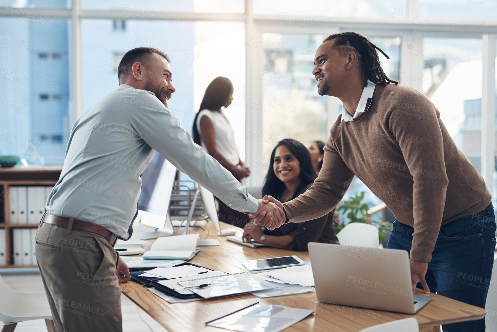 Buy stock photo Cropped shot of two handsome businessmen shaking hands during a meeting in the office during the day