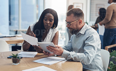 Buy stock photo Cropped shot of two young businesspeople sitting together and discussing in the office while their colleagues work behind them