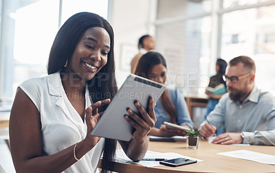 Buy stock photo Cropped shot of an attractive young businesswoman sitting and using a tablet while her coworkers work behind her