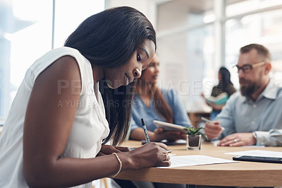 Buy stock photo Cropped shot of an attractive young businesswoman sitting in the office and signing paperwork while her colleagues work behind her