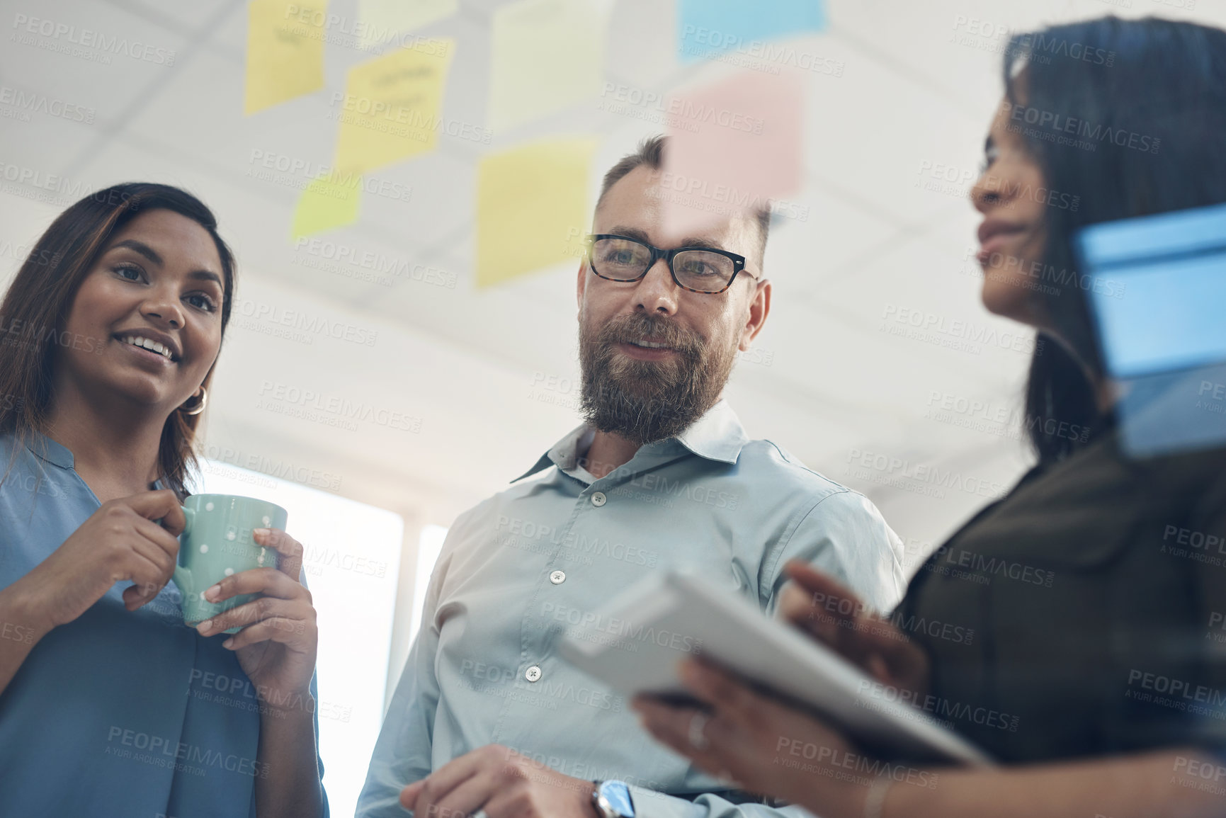 Buy stock photo Cropped shot of a diverse group of businesspeople standing together and using a glass board to brainstorm in the office