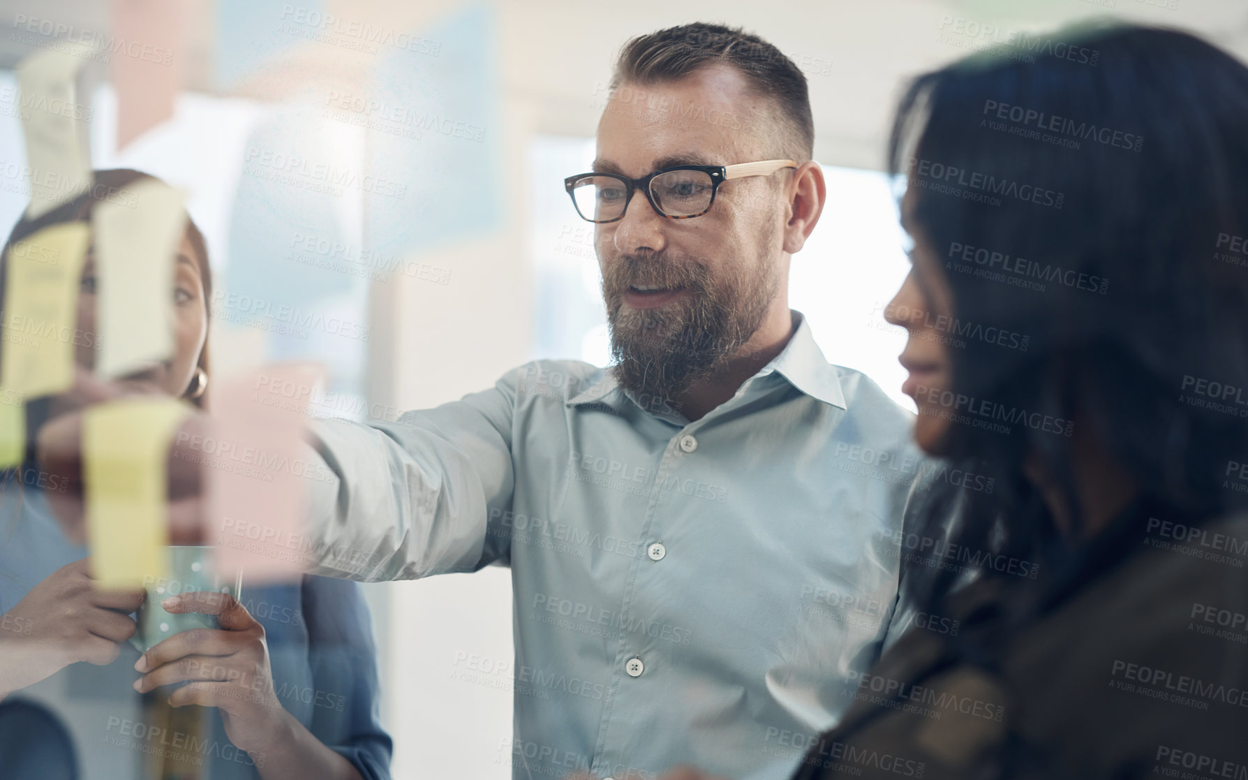 Buy stock photo Cropped shot of a diverse group of businesspeople standing together and using a glass board to brainstorm in the office