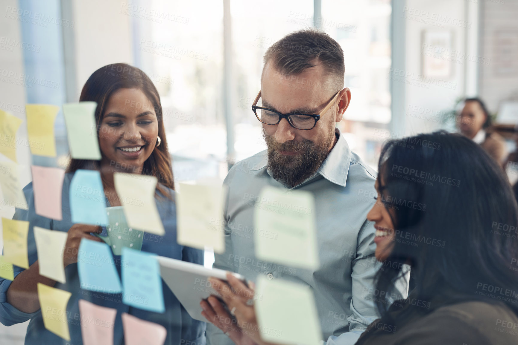 Buy stock photo Cropped shot of a diverse group of businesspeople standing together and using a glass board to brainstorm in the office