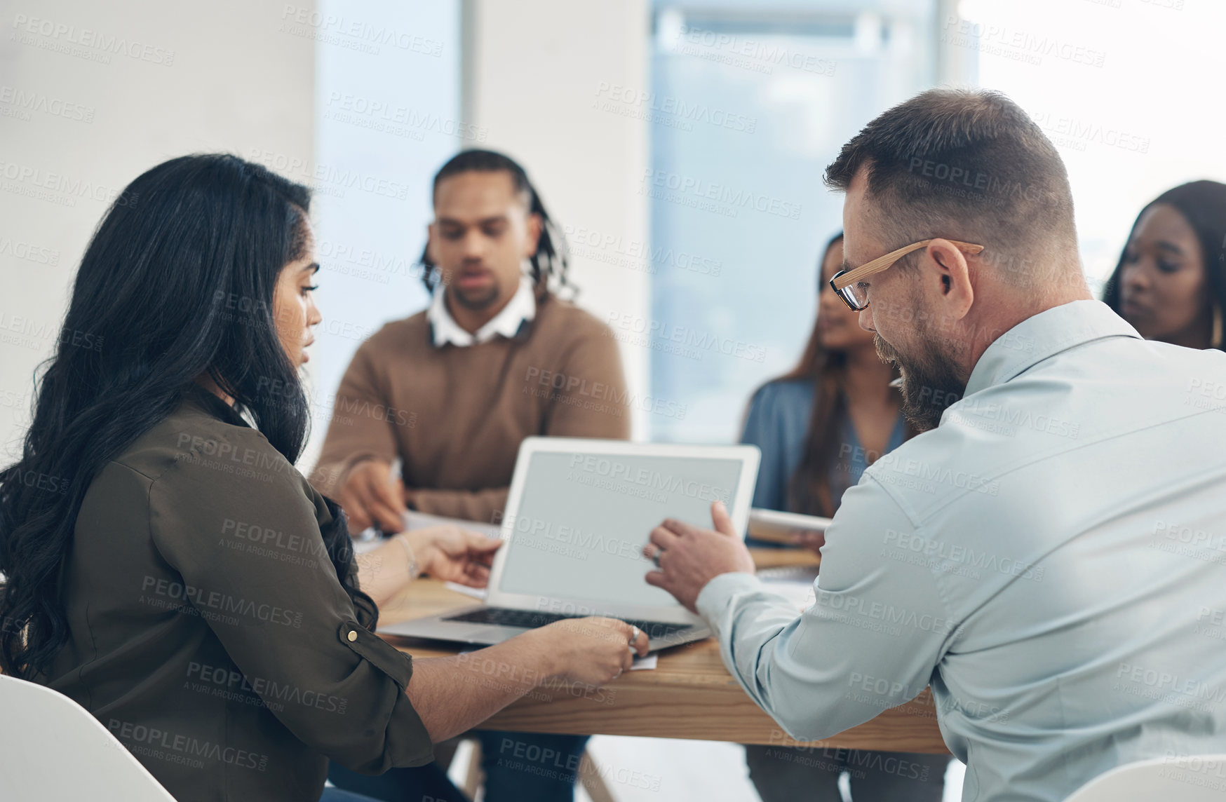 Buy stock photo Cropped shot of a diverse group of businesspeople sitting together and using a laptop during a meeting in the office