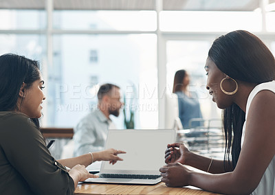 Buy stock photo Cropped shot of a two young businesswomen sitting together and using a laptop while their colleagues work in the background