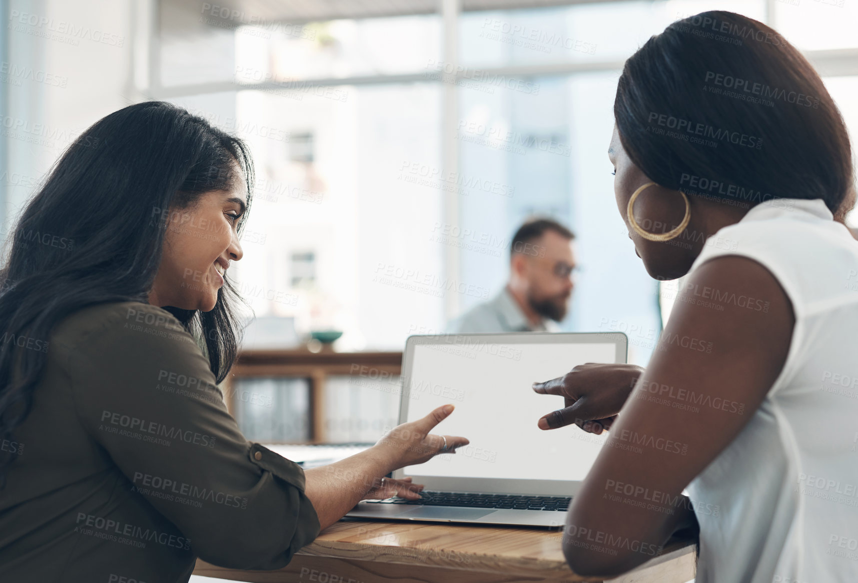 Buy stock photo Cropped shot of a two young businesswomen sitting together and using a laptop while their colleagues work in the background