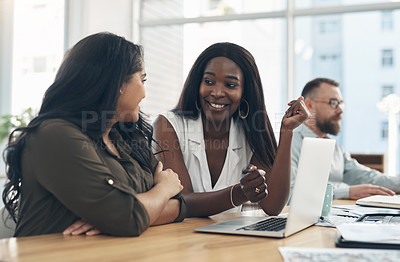 Buy stock photo Cropped shot of two young businesswomen sitting together and using a laptop while their colleagues work in the background