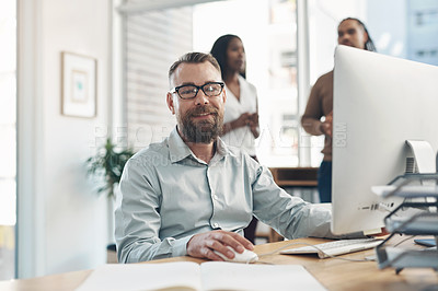 Buy stock photo Cropped portrait of a handsome young businessman sitting and using a computer while his colleagues work in the background