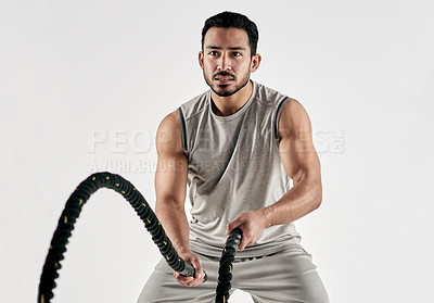 Buy stock photo Studio shot of a muscular young man exercising with battle ropes against a white background